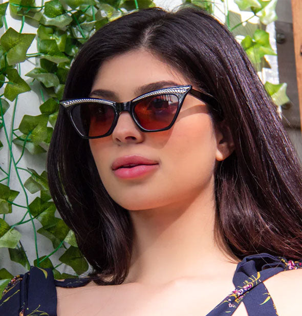 Model wears a pair of black cat-eye sunglasses with silver frame embellishments