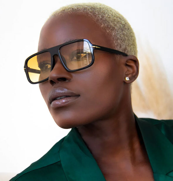 Model wears a pair of black square sunglasses with a gold temple embellishment and yellow lenses