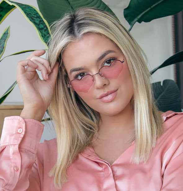 Model wears a pair of pink heart-shaped sunglasses with half rim