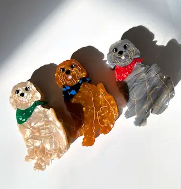 Three quartz-effect Goldendoodle dog hair clips: one apricot with green neckerchief, one amber-brown with blue neckerchief, and one gray streaked with red neckerchief