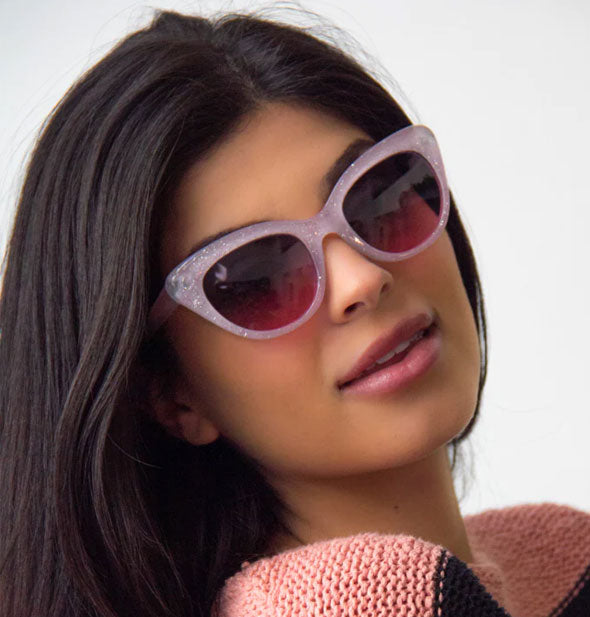 Model wears a pair of glittery purplish cat-eye sunglasses with dark rosy lenses