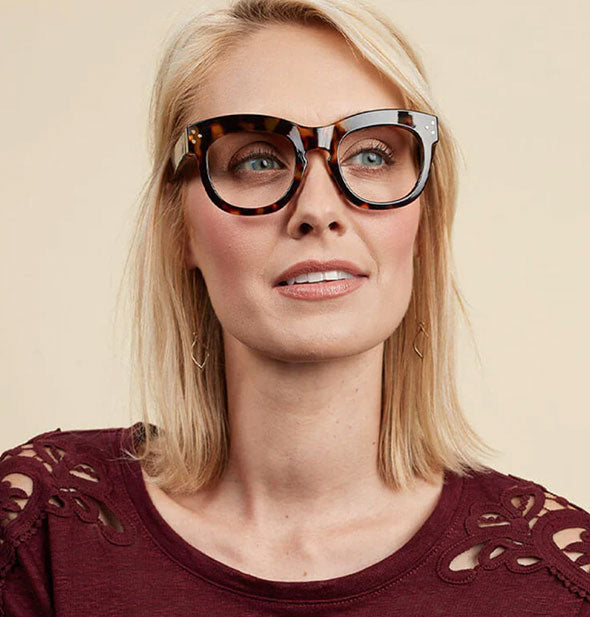 Model wears a pair of thick-rimmed brown tortoise reading glasses with decorative detail at arm hinge