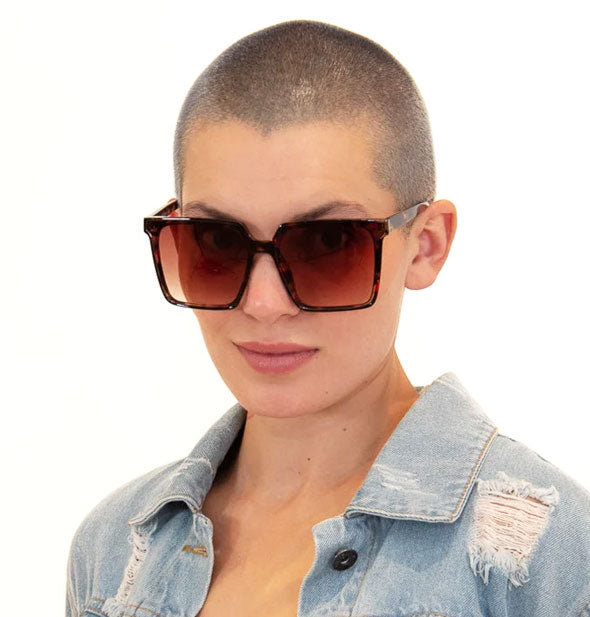 Model with shaved head wears a pair of oversized square brown tortoise sunglasses