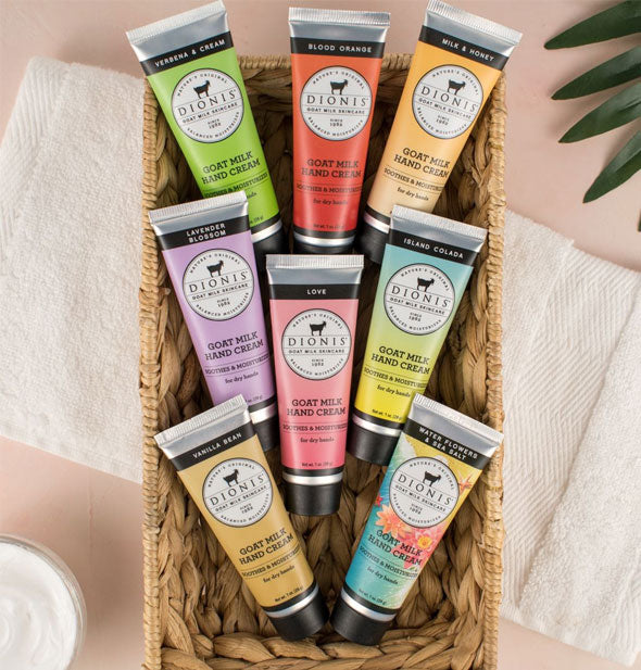 A rectangular basket staged with white towel and plant frond is filled with eight one-ounce bottles of Dionis Goat Milk Hand Cream in an assortment of fragrances