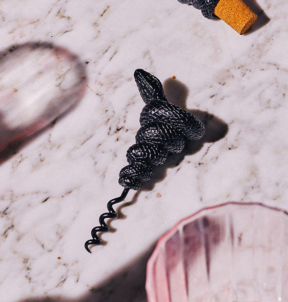 Textured black coiled snake corkscrew rests on a marble countertop