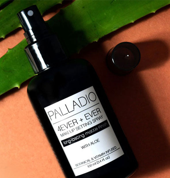 Bottle of Palladio 4Ever + Ever Makeup Setting Spray with cap removed rests on an aloe leaf