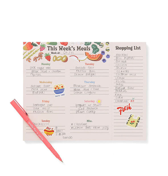 This Week's Meals and Shopping list pad shown filled in and accented with stickers with a pink pen resting on top