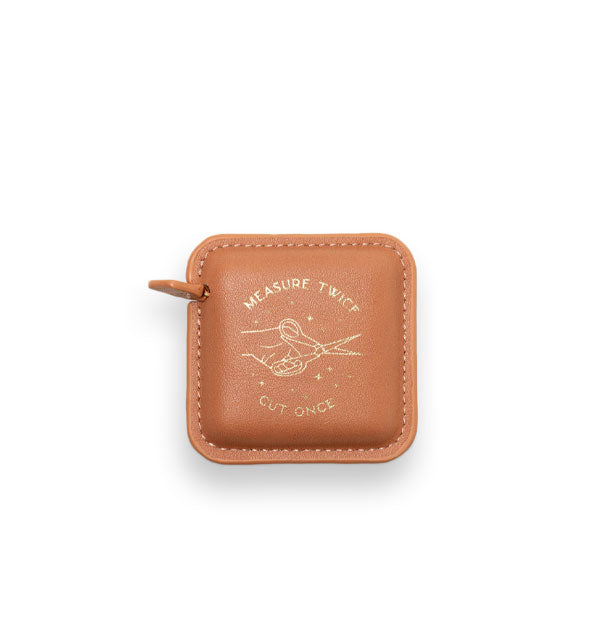 Square stitched salmon-colored measuring tape holster with pull tab features metallic gold foil hand with scissors artwork and, "Measure twice, cut once" lettering accented by stars