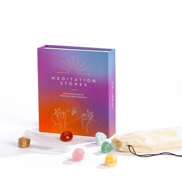 Meditation Stones box kit with blue, purple, and red ombre coloration features white and gold lettering and design accents; included crystals are laid out in the foreground with a white drawstring bag