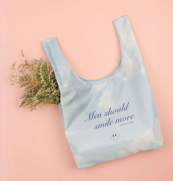 Men Should Smile More tote bag is staged with a bundle of baby's breath