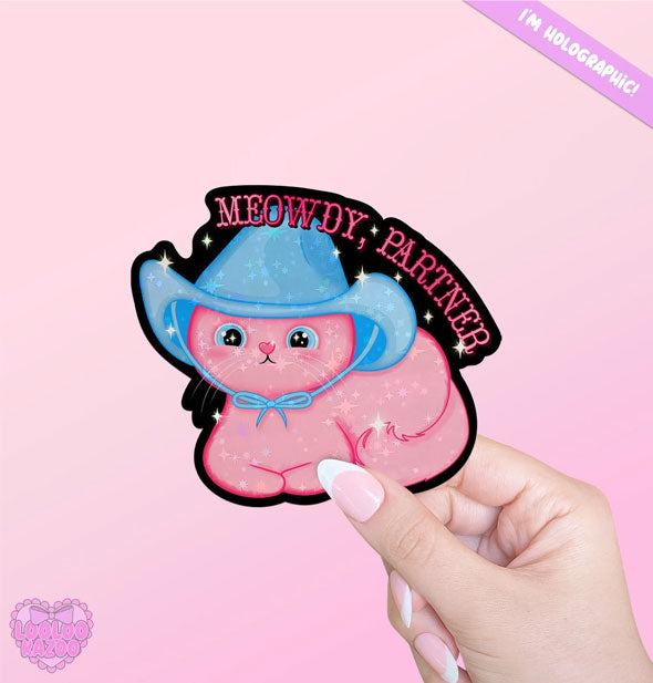 Model's hand holds a sticker with illustration of a pink kitten wearing a blue cowboy hat underneath the words, "Meowdy, partner" in pink Western0style lettering