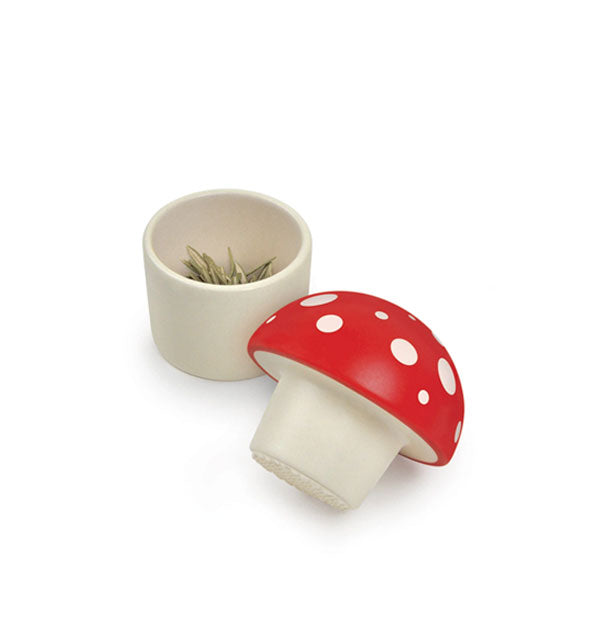 Red and white mushroom-shaped herb grinder shown taken apart to reveal leaves inside
