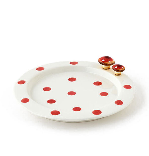 Round white dinner plate features intermittent red spots and two small mushroom figurines on its rim