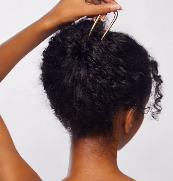 Model sticks a gold hair pin into a twist updo