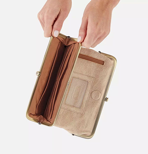 Model's hands hold open the pocket of a metallic gold leather wallet to reveal a brown interior with card slots