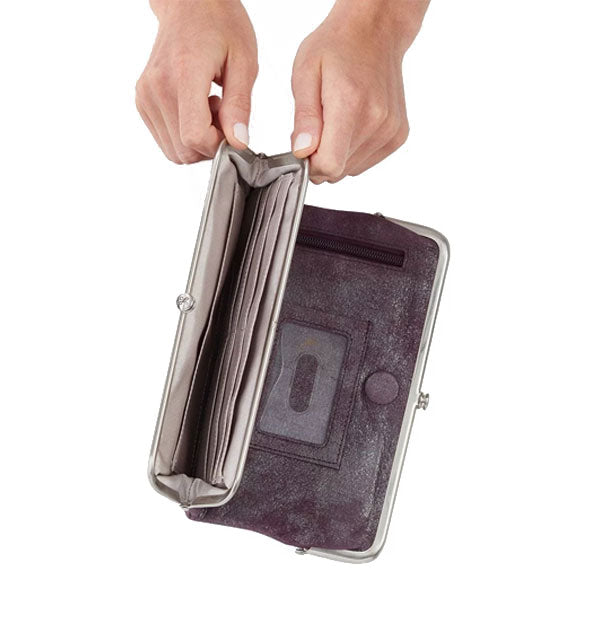 Model's hands hold open a frame compartment of a Hobo wallet to show storage inside