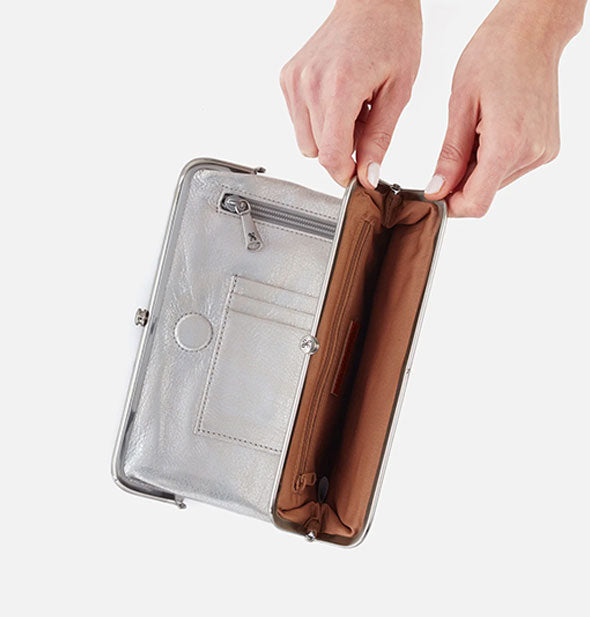 Model's hands hold open a section of a metallic silver leather wallet to reveal brown interior with additional zipper pocket