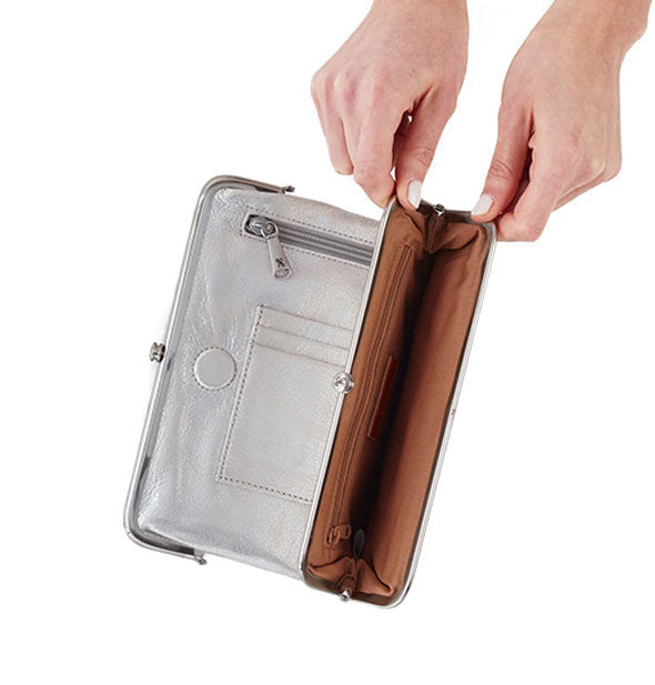 Model's hands hold open a section of a metallic silver leather wallet to reveal brown interior with additional zipper pocket