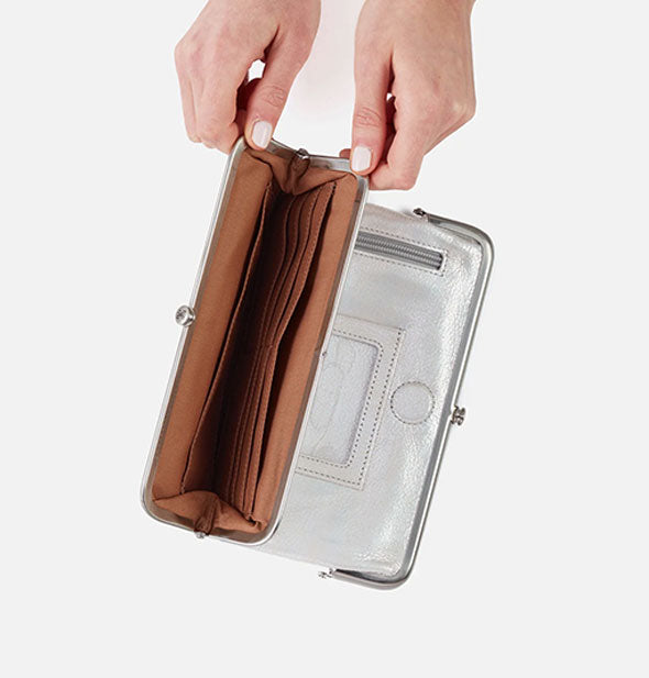 Model's hands hold open the pocket of a metallic silver wallet to reveal brown interior with card slots