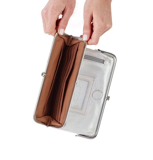 Model's hands hold open the pocket of a metallic silver wallet to reveal brown interior with card slots