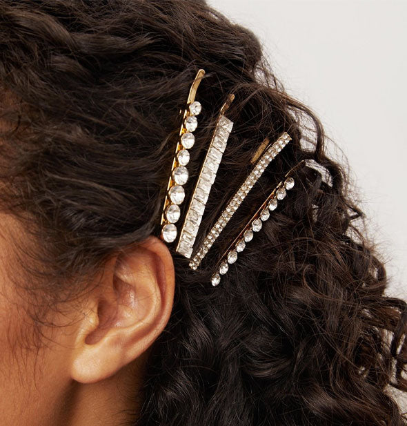 Model wears four gold-toned rhinestone-encrusted bobby pins in a side-swept hairstyle