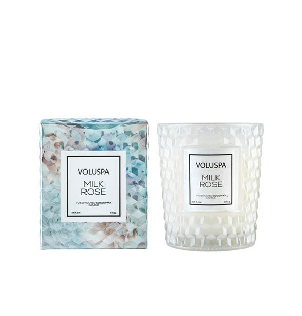 Frosted white embossed glass Voluspa Milk Rose candle jar next to decorative blue and grey gift box with rose print