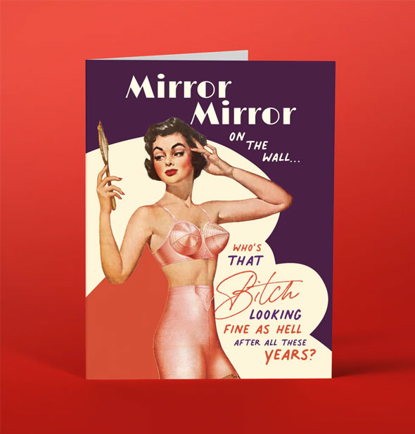 Greeting card on red background features retro pinup-style model in pink lingerie gazing into a hand mirror alongside the message, "Mirror mirror on the wall...who's that bitch looking fine as hell after all these years?"