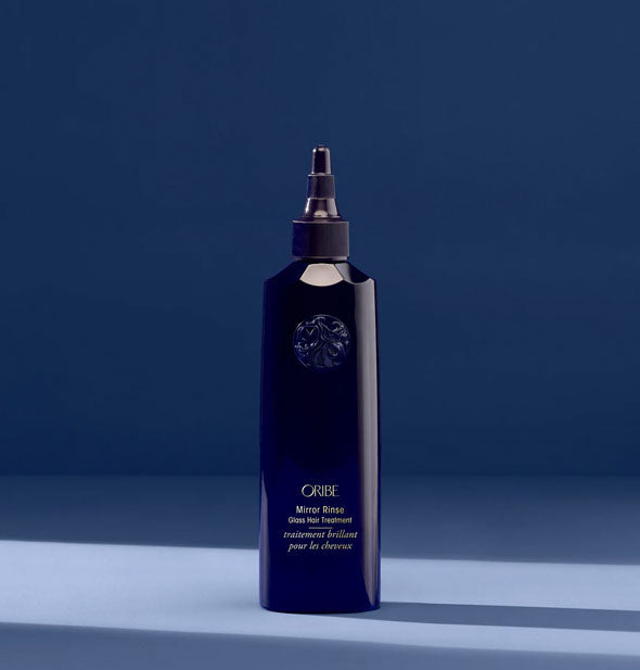 Dark blue 5.9 ounce bottle of Oribe Mirror Rinse Glass Hair Treatment on a dark blue shadowy backdrop