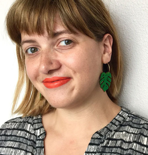 Smiling model wears a green monstera leaf hoop earring