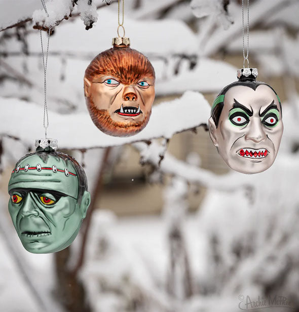 Frankenstein, werewolf, and vampire ornaments hung from a snowy tree branch
