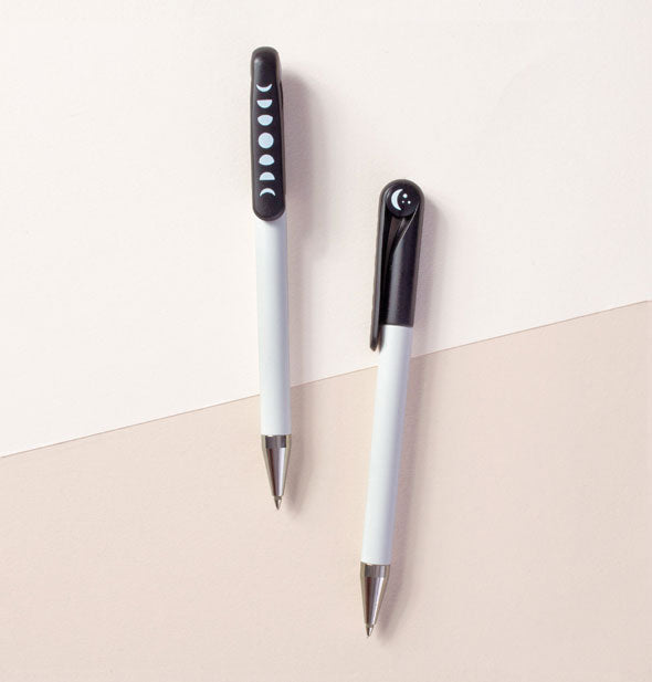 Two pens with white bottom halves and black top halves imprinted with white moon phase graphics