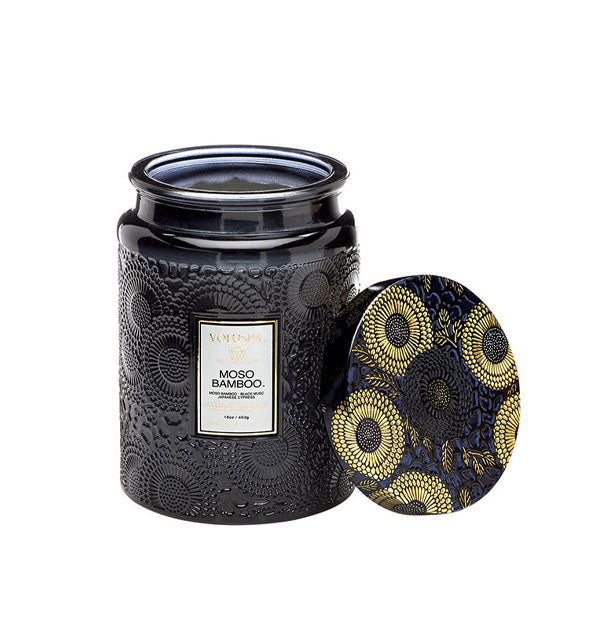 Black embossed glass Moso Bamboo Voluspa jar candle with black and gold metallic floral lid set to the side