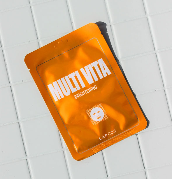 Orange Multi Vita Brightening mask packet by Lapcos rests on white tile