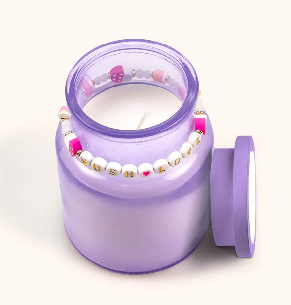 Opened purple glass candle jar with "Mush Love" beaded bracelet around its neck