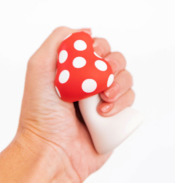 Model's hand squeezes a red and white foam mushroom de-stress toy