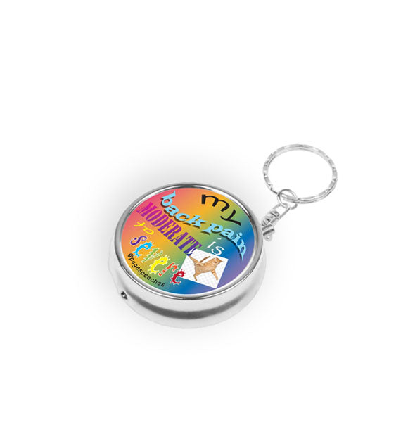 Round silver pill case with keychain says, "My back pain is moderate to severe" in alternating typefaces on a rainbow backdrop with small image of a contorted cat