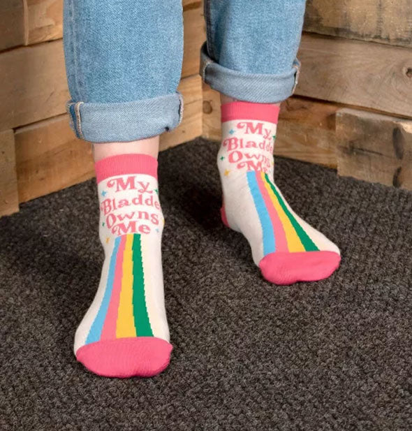 Model wears a pair of My Bladder Owns Me ankle socks on a carpeted surface in front of a wooden backdrop