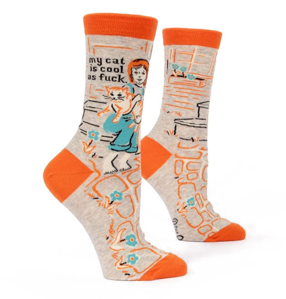 Pair of beige crew socks with orange toes, heels, and top bands feature all-over illustration including a girl holding a cat near the caption, "My cat is cool as fuck" printed in black lettering