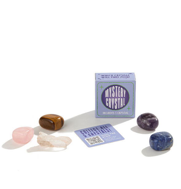 Small periwinkle box labeled "Mystery Crystal" in staged with a matching card printed with QR code and five stones: clear quartz, rose quartz, tiger eye, sodalite, and amethyst