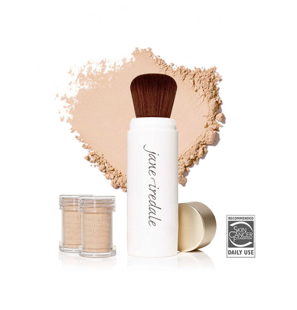 White Jane Iredale powder brush with gold cap removed and set to the side, two refill canisters nearby, and an enlarged product sample in the background in shade Natural