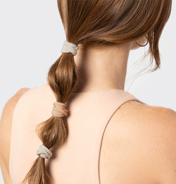 Model wears three hair elastics in neutral shades in a low ponytail