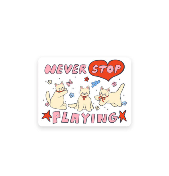 Rectangular white sticker with rounded corners features illustration of three white kittens in red bows surrounded by flowers, butterflies, and birds, and the words, "Never stop playing" in pink lettering accented by a red heart and stars