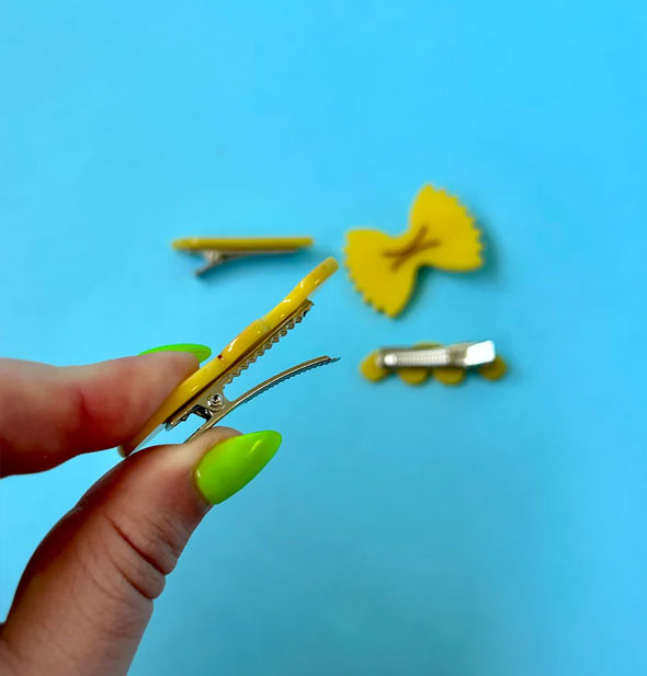 Model holds open the clamp of a pasta-shaped hair clip with others from the set visible in the background