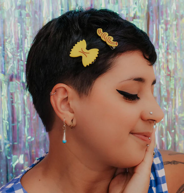 Smiling model wears two pasta-shaped hair clips at the side of a pixie cut