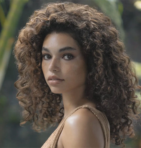 Model with voluminous curly hair poses in front of a tropical backdrop