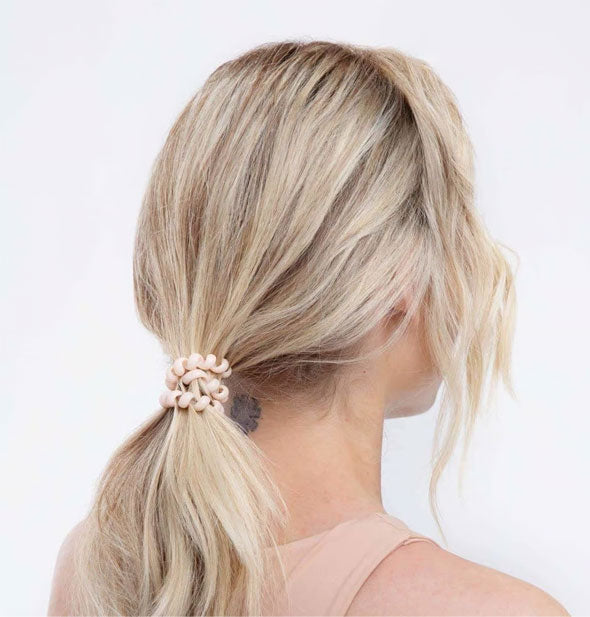Model wears a whitish-pink coil in a low ponytail