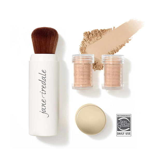 White Jane Iredale powder brush, two clear refill canisters, and gold cap are spaced out with a sample of swiped powder sunscreen in shade Nude