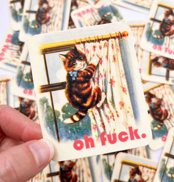 Model's hand holds an Oh Fuck kitty sticker in front of a pile of others like it