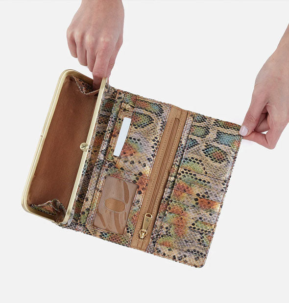 Model's hands hold open a multicolored snakeskin print leather trifold wallet with brown lining and gold hardware