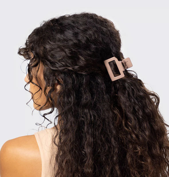 Model with curly dark brown hair wears a rectangular beige open shape claw clip in a half-up style